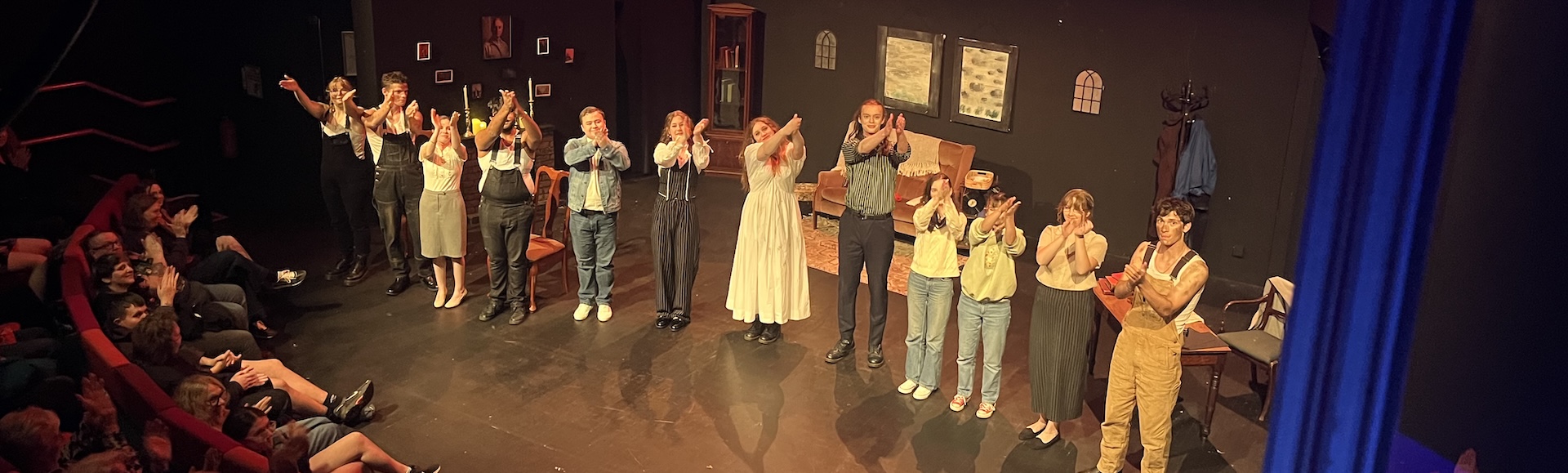 A group of actors bowing at the end of a show inside a theatre, photo taken from up in the high stalls.