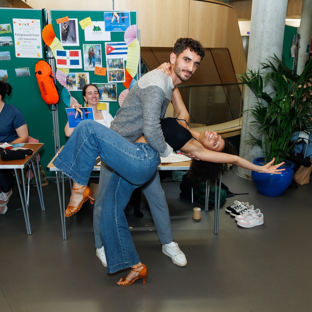 Two students at a societies fair in a dance pose, the guy is holding the girl who is bending backwards.