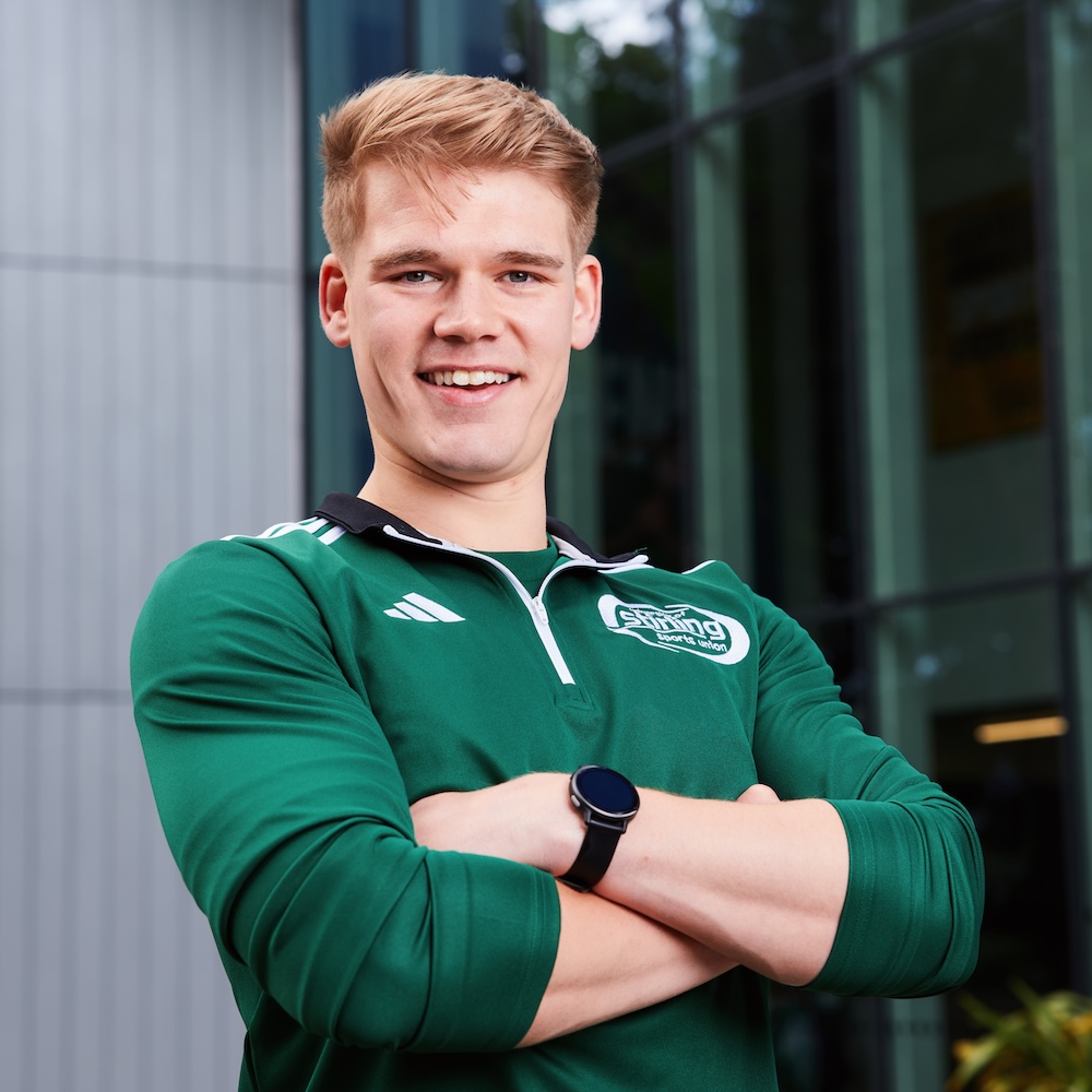 Person with short blonde hair wearing a green sports top 