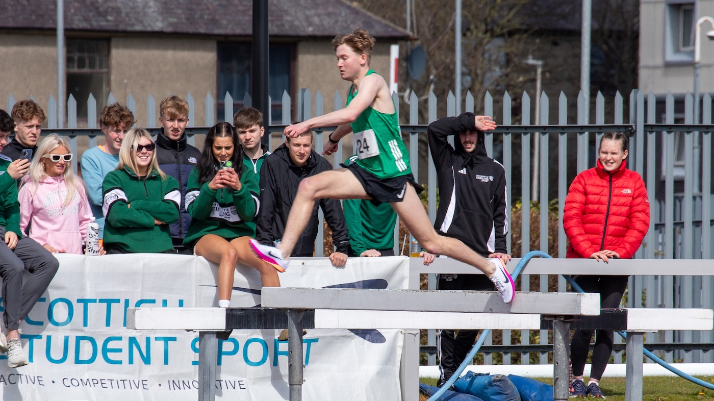 A person wearing sports wear jumping over a sprint jump with spectators behind them