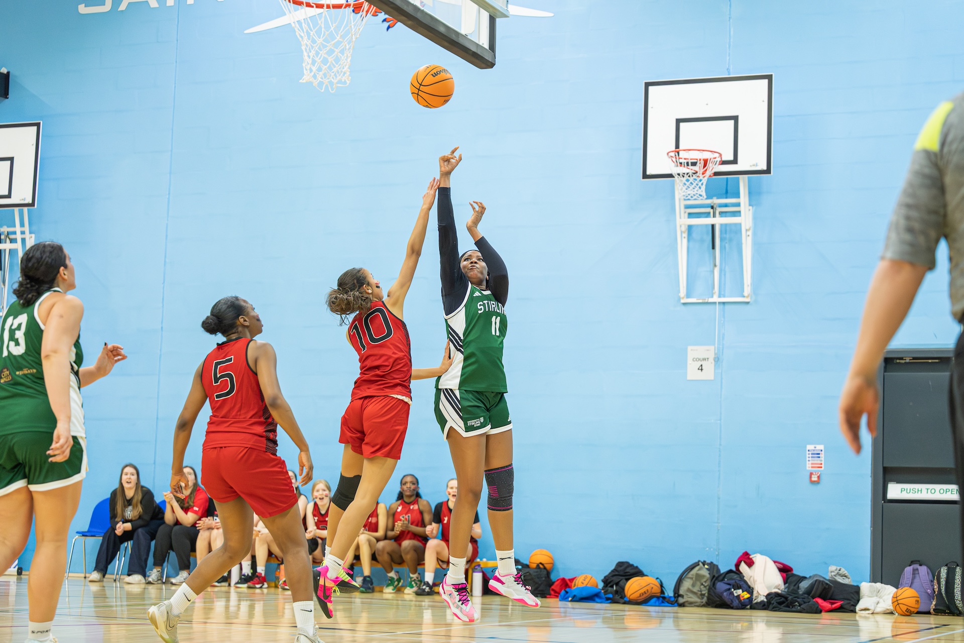 Three people jumping in the air to catch a basketball on an indoor court