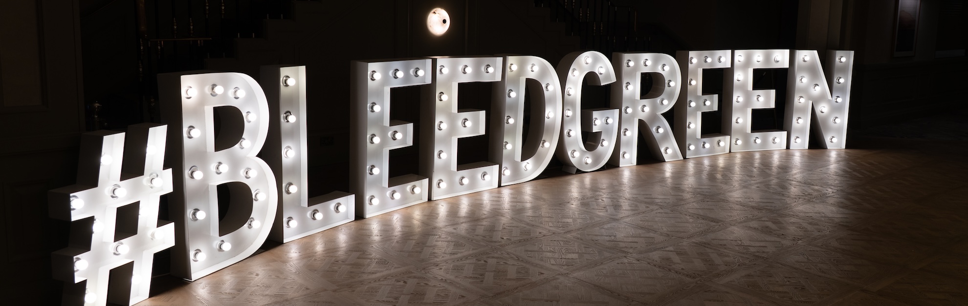 Large light bulb sign that reads #BLEEDGREEN against a black background