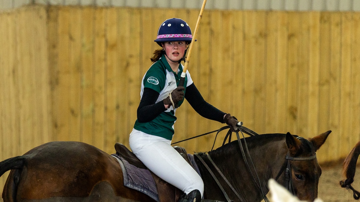 Person riding a horse with white riding trousers and a green Stirling Sports Union branded top