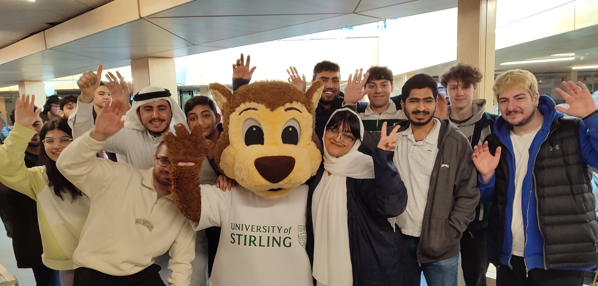 Large group of people all smiling at the camera, in the centre is someone wearing a University of Stirling branded mascot costume.