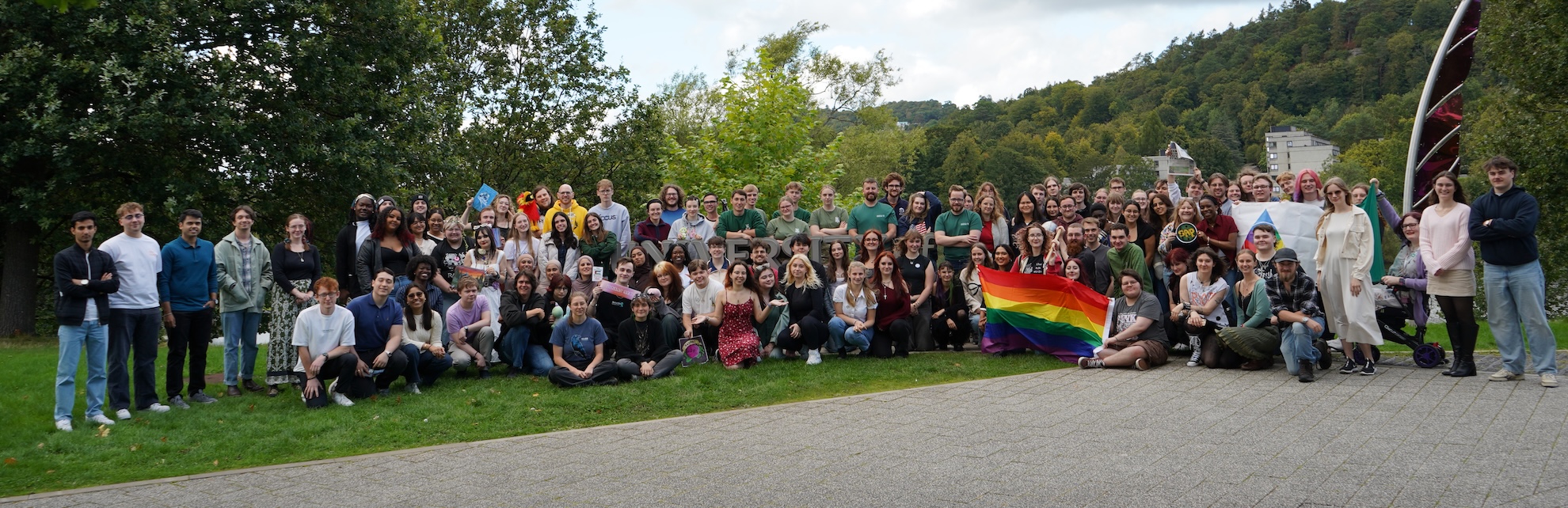 Over 100 people stood in a group for a photo, they are outside on a grass verge.