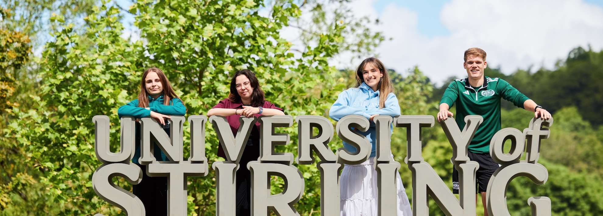 Four people stood behind a sign outside in a garden that reads "University of Stirling"