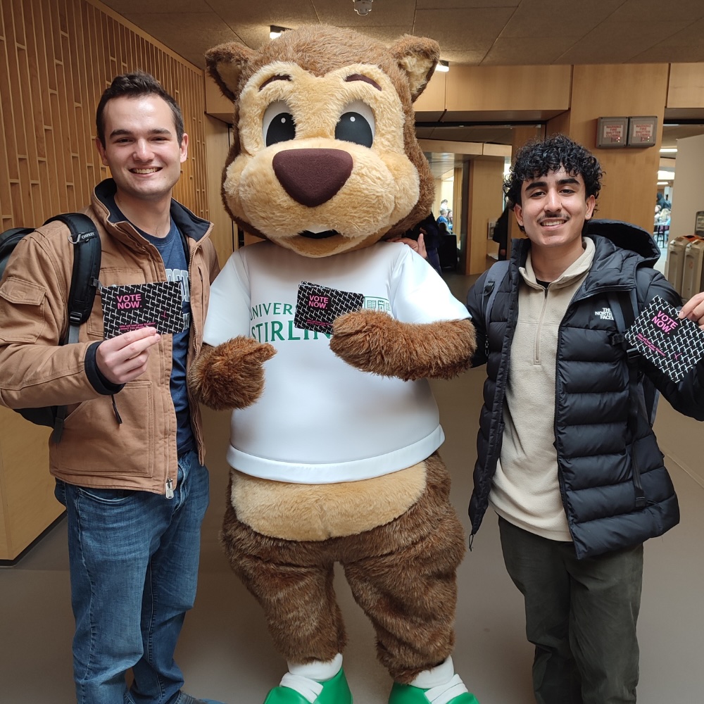 Two people stood either side someone wearing a big fluffy bear costume