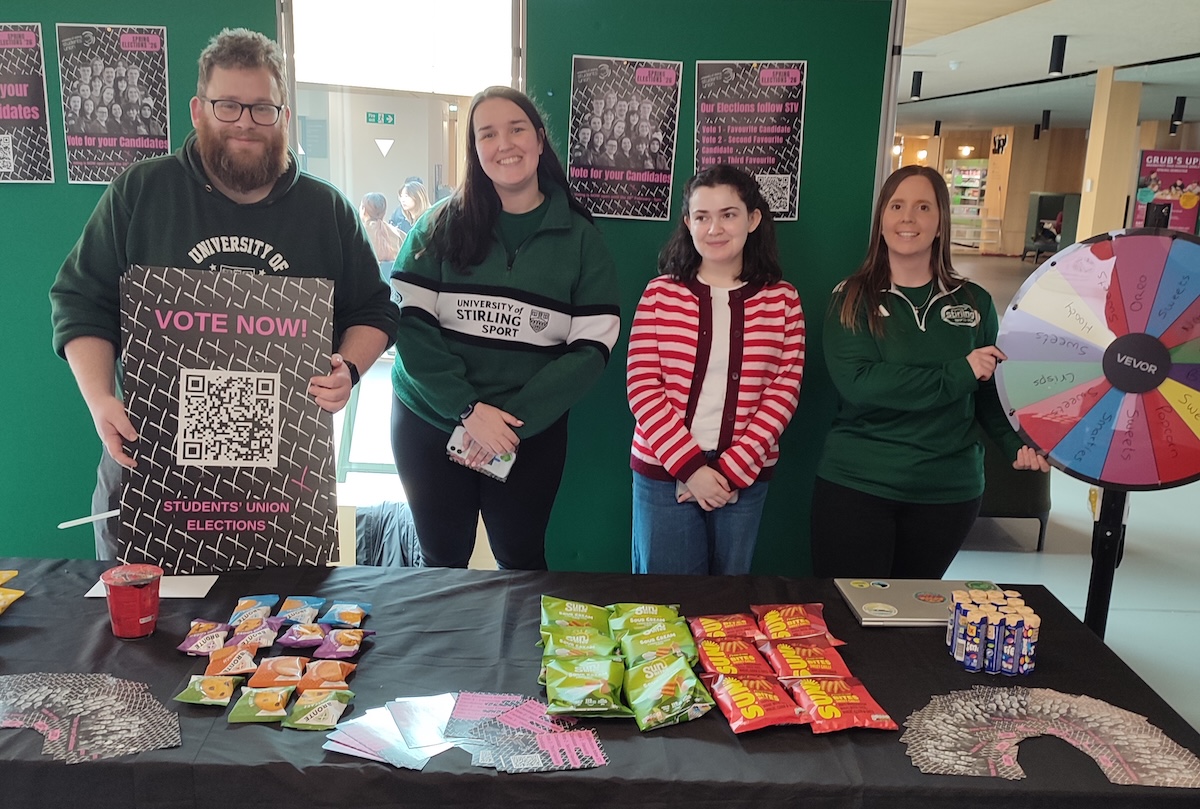 Four people stood behind a desk promoting a students' union election.