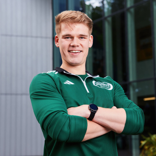 person with short blonde hair wearing a green sports top with folded arms smiling at the camera
