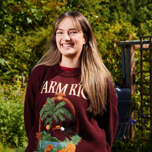 Person with shoulder length light brown hair wearing a Burgundy sweater smiling at the camera. 