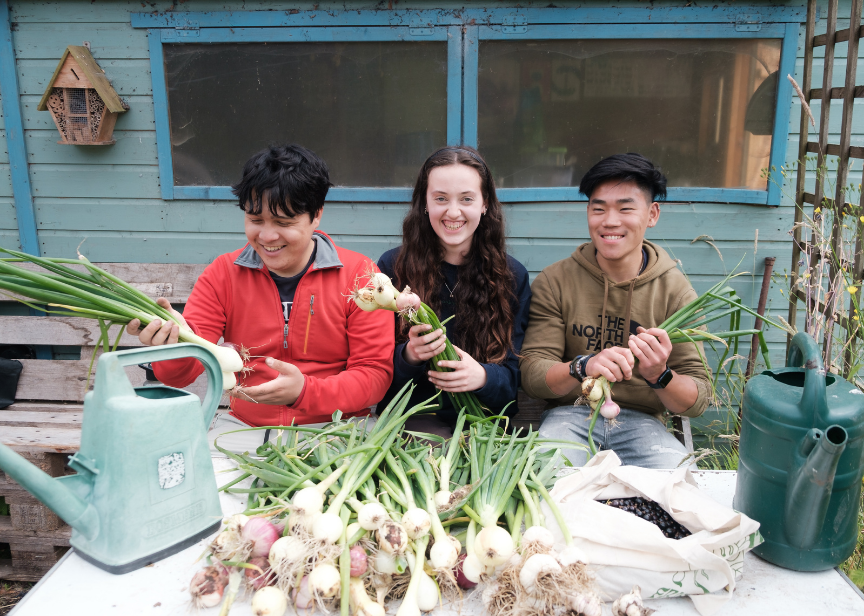 Group of young people happily holding veg harvested from the community garden